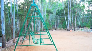 A green swing set in a forested area with dirt ground. - Nature Castle-A traditional kerala style  (Vattavada)