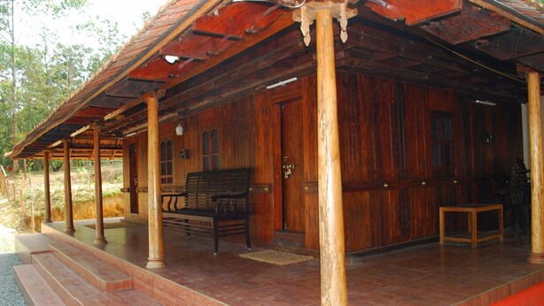 A wooden building with a covered porch, steps leading to the entrance, and a bench inside. - Nature Castle-A traditional kerala style  (Vattavada)