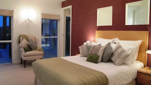 Ein Hotelzimmer mit einem großen Bett, einem Sessel, einem Schreibtisch und Blick ins Freie.