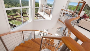 Ein modernes Interieur mit einer Holzspirale, großen Fenstern mit Blick auf eine üppige Landschaft und einer Sitzecke mit Aussicht.