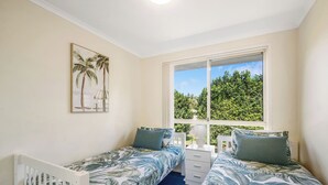 Un dormitorio con dos camas individuales, una mesita de noche, una ventana con vistas a la vegetación y un cuadro colgado en la pared.