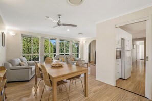 A modern living room with a dining area, large windows, and a ceiling fan.