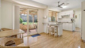 Una cocina moderna con una isla central, un comedor con mobiliario de mimbre y una puerta corrediza de vidrio que da a un patio.