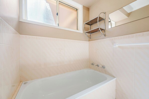 A bathroom with a bathtub, a window, and a metal shelf.