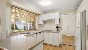 Una cocina moderna con armarios blancos, encimera de granito, horno empotrado y ventana con persianas.