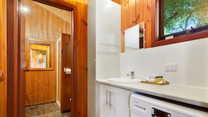 A compact hotel bathroom with a washing machine, a sink, and a mirror.