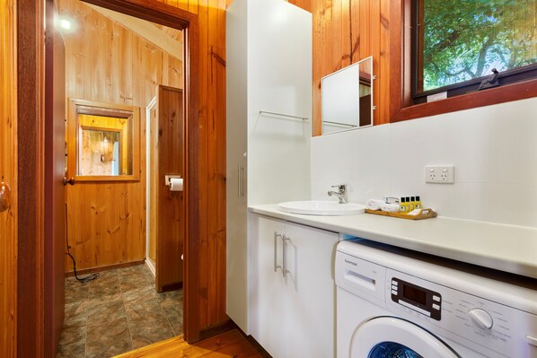 A compact hotel bathroom with a washing machine, a sink, and a mirror.