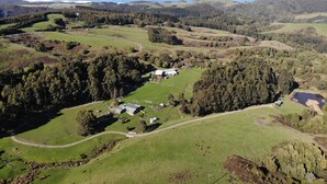 An aerial view of a rural landscape with rolling hills, a small farmstead, and a body of water in the distance.