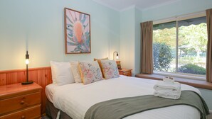 Une chambre d’hôtel avec un lit, une table de chevet, une lampe de chevet, une fenêtre avec des rideaux et un tableau au mur.