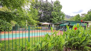 Un espace piscine doté d’un coin salon abrité, entouré d’une végétation luxuriante et d’arbres.