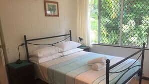 Una cama individual con estructura metálica, una mesita de noche con lámpara y una ventana con vistas a zonas verdes.