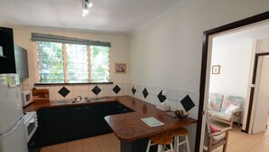 Cocina compacta con pileta, microondas y refrigerador. Hay una ventana con persianas, una silla y una puerta que conduce a otra habitación.