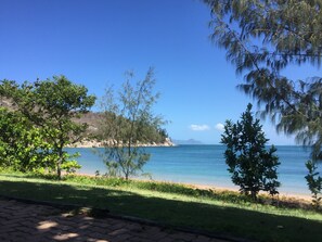 A coastal view with a clear sky, a sandy beach, and lush greenery. - Wheelchair Accessible with Assistance Cottage in a peaceful place. (Nelly Bay)
