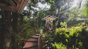 A garden pathway leading to a wooden pergola surrounded by lush tropical plants. - Secluded Hillside Cottage with Bay & Rainforest Views, Just 5 Mins to the Beach (Englishman's Bay)