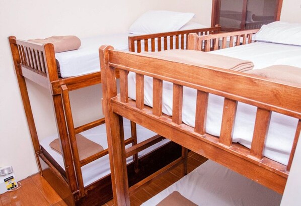 A room with three wooden bunk beds, each with a pillow and white bedding.