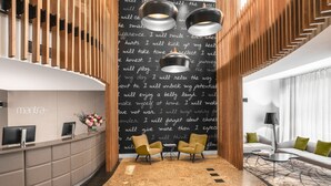 A modern reception area with a curved desk, two armchairs, a black wall with motivational text, and a wooden slatted ceiling.