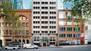 A multi-story building with a central entrance, surrounded by other buildings.