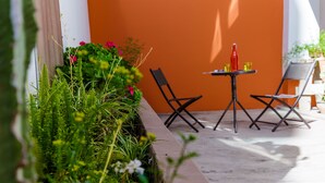Eine Terrasse mit Tisch und Stühlen, umgeben von üppiger Vegetation und einer leuchtend orangefarbenen Wand.