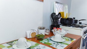 Eine Küche mit Herd, Töpfen und Kochgeschirr. Ein Tisch mit Tischdecke, einer weißen Tasse und einer Schüssel.