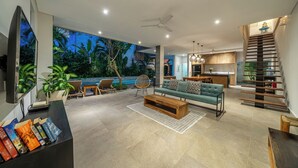 A modern living room with a sofa, coffee table, and books. There is a staircase with a railing and a kitchen area with a countertop and cabinets. - Villa Jekumah 3 - 1 minute walk to restaurants (Kerobokan)
