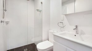 Un bagno moderno con doccia vetro, un water bianco e un lavandino bianco con specchio sopra.