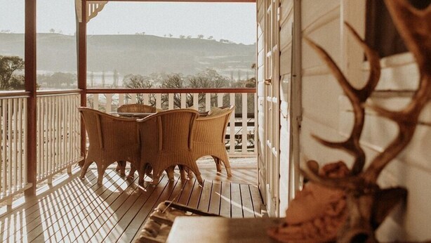 A covered porch with a table and chairs, a large antler decoration, and a view of the landscape.