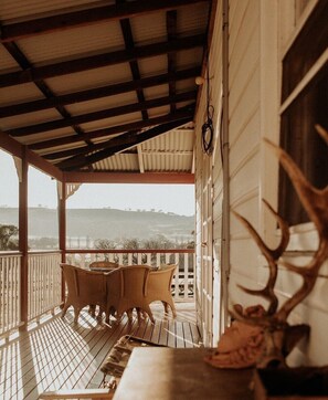 A covered porch with a table and chairs, a large antler decoration, and a view of the landscape. - Stockmans Cottage - historic rural property (via Glen Innes)