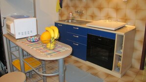 Eine kompakte Küche mit Mikrowelle, Spüle und Geschirrspüler. Ein Tisch mit Obstschale und Unterlage ist ebenfalls vorhanden.