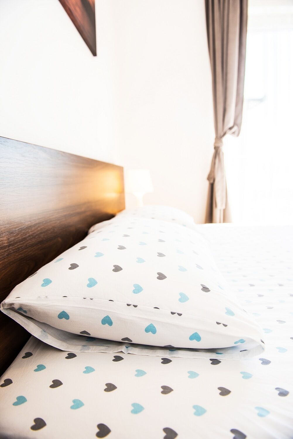 A neatly made bed with patterned bedding, a wooden headboard, and a window with curtains.