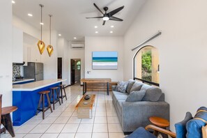 Una cocina moderna con barra, zona de estar con sofá y mesa de centro, y un ventanal con vistas.