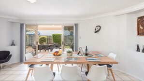 A dining area with a wooden table, white chairs, and a view through glass doors to an outdoor patio. - Kidman Place - Spacious Luxury+ FREE WIFI + WINE (Brisbane North)