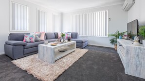 A modern living room with grey sofas, a white coffee table, and a grey carpet. - Kidman Place - Spacious Luxury+ FREE WIFI + WINE (Brisbane North)