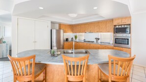 A modern kitchen with a central island, wooden cabinets, stainless steel appliances, and a white ceiling. - Kidman Place - Spacious Luxury+ FREE WIFI + WINE (Brisbane North)