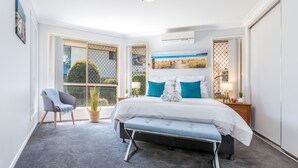 A bedroom with a large bed, a bench, a chair, and a window with a view of greenery. - Kidman Place - Spacious Luxury+ FREE WIFI + WINE (Brisbane North)