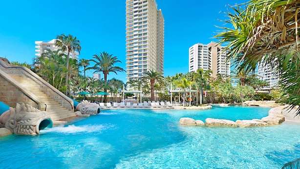 A resort pool with a water slide, palm trees, and high-rise buildings in the background.