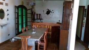A dining area with a table and chairs, a green-lit door, and a wall decoration. - Vacation home with pool, fan, barbecue, Wi-Fi, and air conditioning. (Ubatuba)