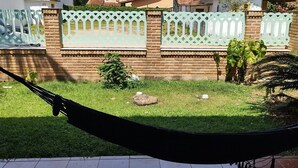 A hammock on a tiled patio with a view of a brick wall and houses in the background. - Vacation home with pool, fan, barbecue, Wi-Fi, and air conditioning. (Ubatuba)