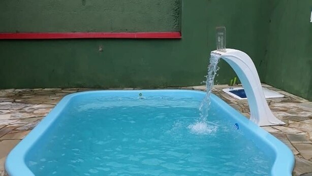 A blue above-ground pool with a water spout, surrounded by stone tiles. - Vacation home with pool, fan, barbecue, Wi-Fi, and air conditioning. (Ubatuba)