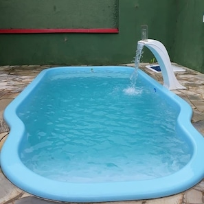 A blue above-ground pool with a water spout, surrounded by stone tiles. - Vacation home with pool, fan, barbecue, Wi-Fi, and air conditioning. (Ubatuba)