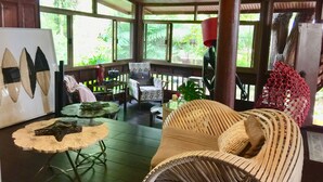 A spacious room with a wooden ceiling, large windows, a wicker sofa, a round table, and a chair.