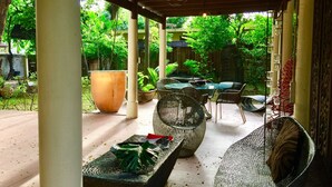 An outdoor patio with a glass table, wicker chairs, and a large planter.