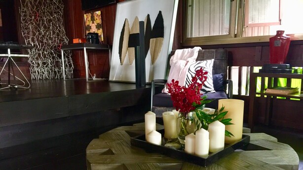 A cozy living area with a wooden coffee table holding candles and flowers, a sofa with cushions, and a decorative wall piece.
