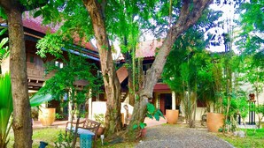 A pathway leading to a building with a red roof, surrounded by trees and potted plants.