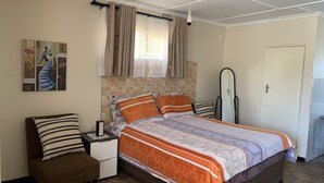 A bedroom with a bed, nightstand, chair, and a painting on the wall.