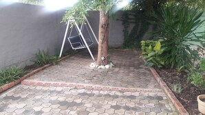 A paved patio with hexagonal tiles, a swing set, and various plants.