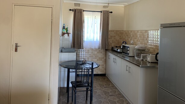 A compact kitchen with a dining table and chairs, a refrigerator, and a microwave.