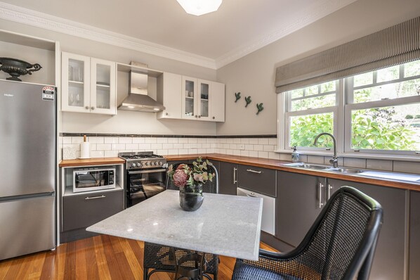 A modern kitchen with a dining table, chairs, a refrigerator, oven, microwave, and cabinets.