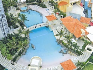 Relax by the resort's central pool surrounded by palm trees and a picturesque bridge.
