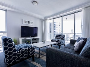 Relax in this stylish living room with a flat-screen TV, coffee table, and two comfortable armchairs, taking in the city view.