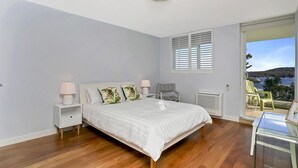 Une chambre à coucher avec un lit, des tables de chevet, une fenêtre avec des volets et une vue sur la mer.